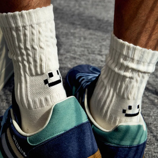 White socks with smiley face design worn with blue and green shoes on a gray pavement background.