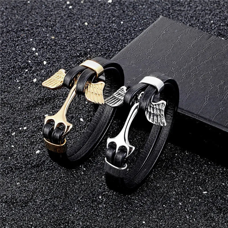 Black leather bracelets with gold and silver winged charms on a dark textured surface.