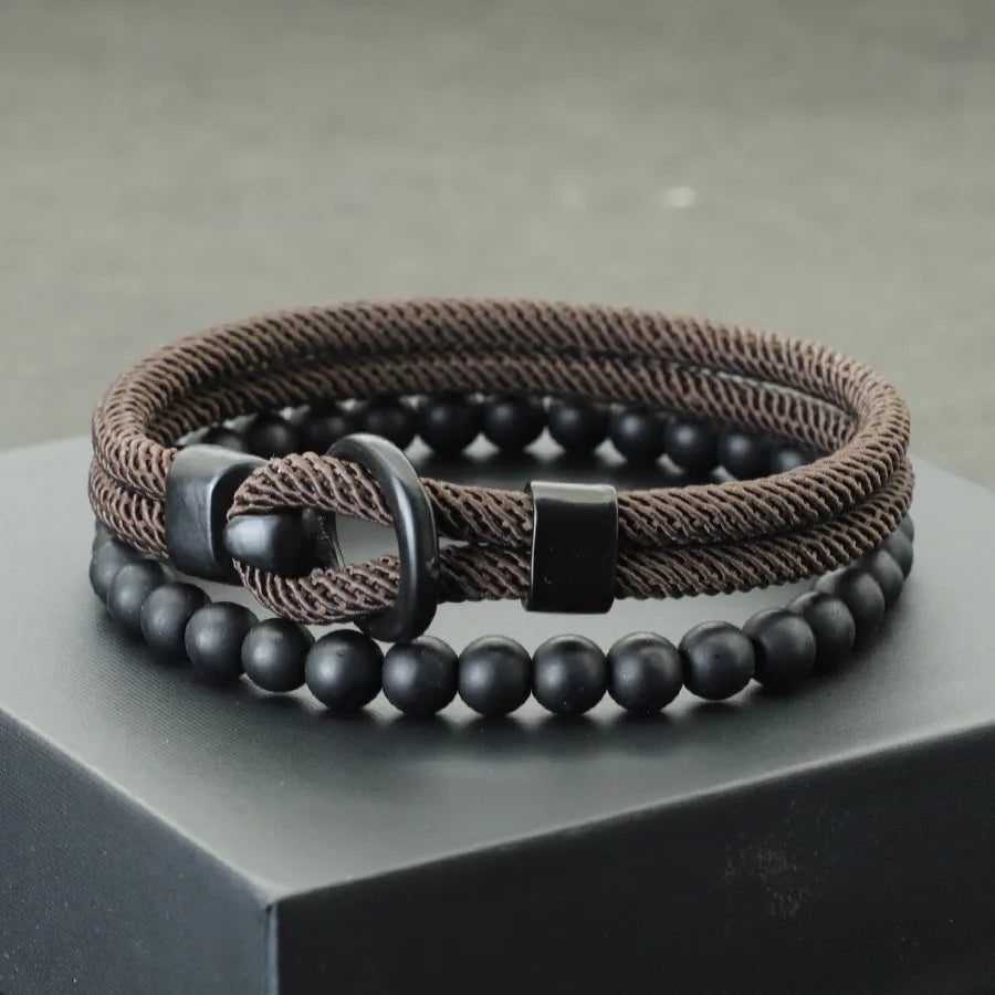A brown leather bracelet with black onyx stones and a minimalist design, displayed on a textured background.