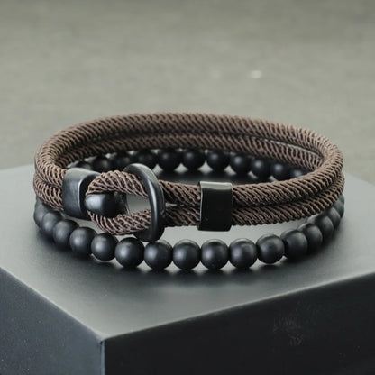 A brown leather bracelet with black onyx stones and a minimalist design, displayed on a textured background.
