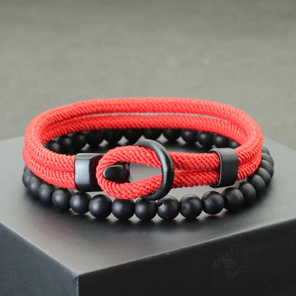 A red and black bracelet with a combination of smooth black beads and a textured red cord, displayed on a gray platform.